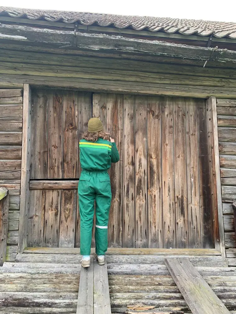 Bildet viser ei ung kvinne som låser en låvedør. Hun har på seg en heldress.