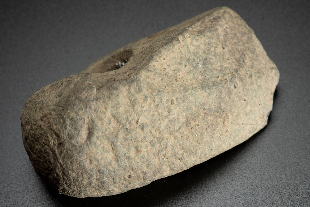 Fragment av skafthålsyxa av grönsten. Yxan skuren i sin längdriktning, mitt itu. Brottytan går diagonalt från undersidan till ovansidan. Obetydligt slipad. Omkring halva yxan är avslagen.