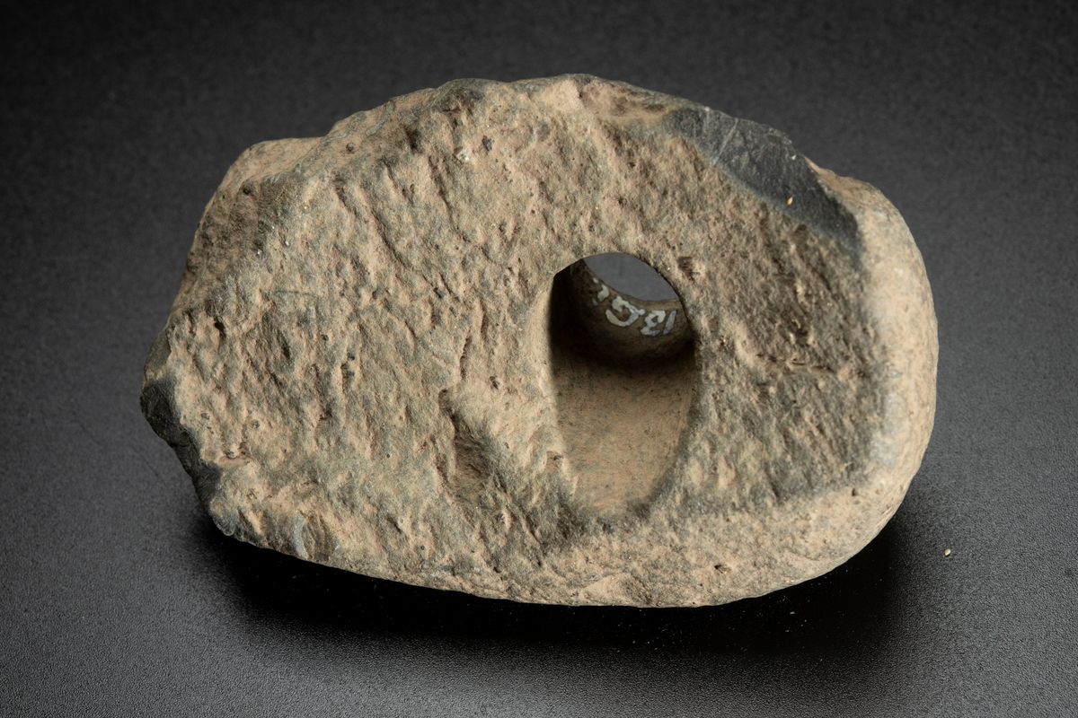 Fragment av skafthålsyxa av grönsten. Yxan skuren i sin längdriktning, mitt itu. Brottytan går diagonalt från undersidan till ovansidan. Obetydligt slipad. Omkring halva yxan är avslagen.