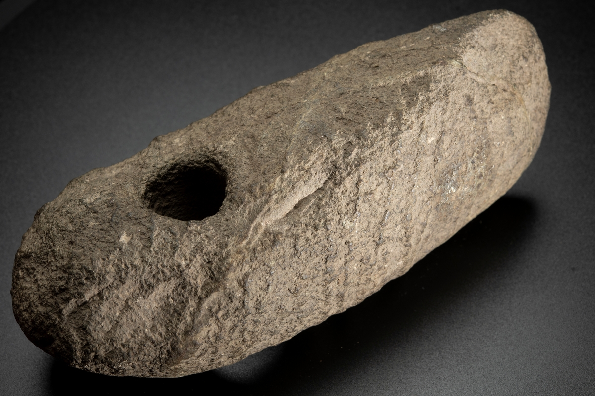 Skafthålsyxa av bergart. Av grovkornig, ådrig bergart. Ett klumpigt, oslipat exemplar.