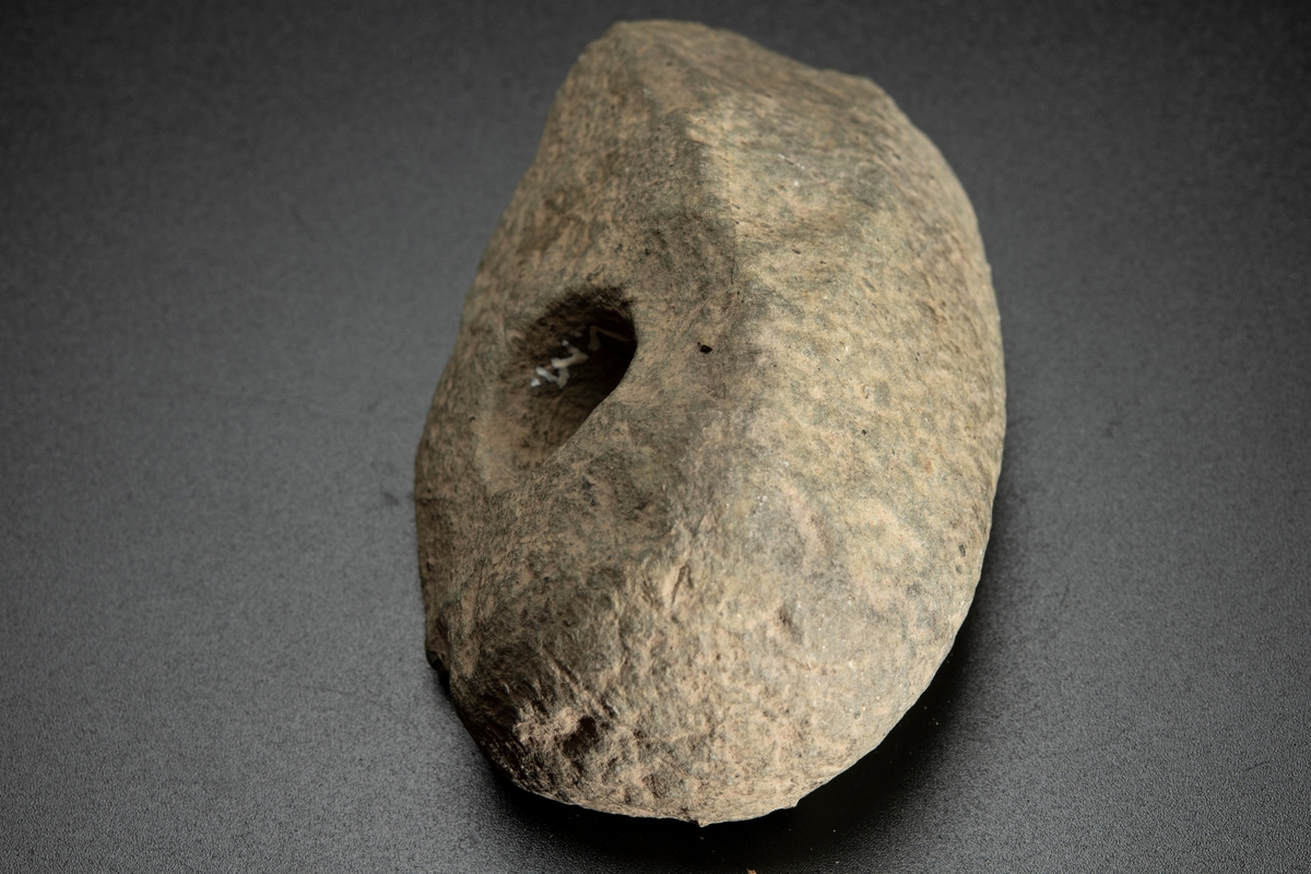 Fragment av skafthålsyxa av grönsten. Yxan skuren i sin längdriktning, mitt itu. Brottytan går diagonalt från undersidan till ovansidan. Obetydligt slipad. Omkring halva yxan är avslagen.