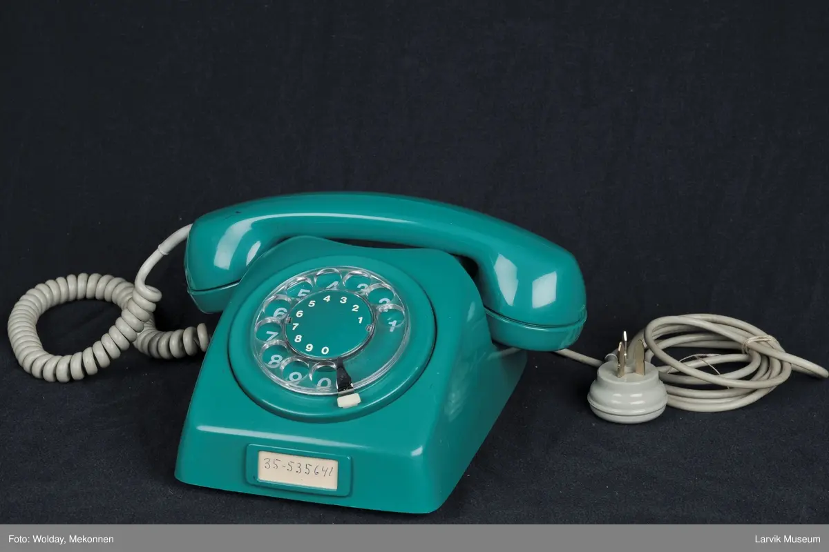 Bordtelefon med midtstil rund tallskive og telefonrør liggende i overkant. Vanlig modell