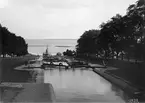 Panorama över den mäktiga Karl Johan-slussen en sommarkväll 1903. På väg uppför slusstrappan skymtar S/S Per Brahe, som gått till historien för sin dödsbringande förlisning utanför Hästholmen 1918.