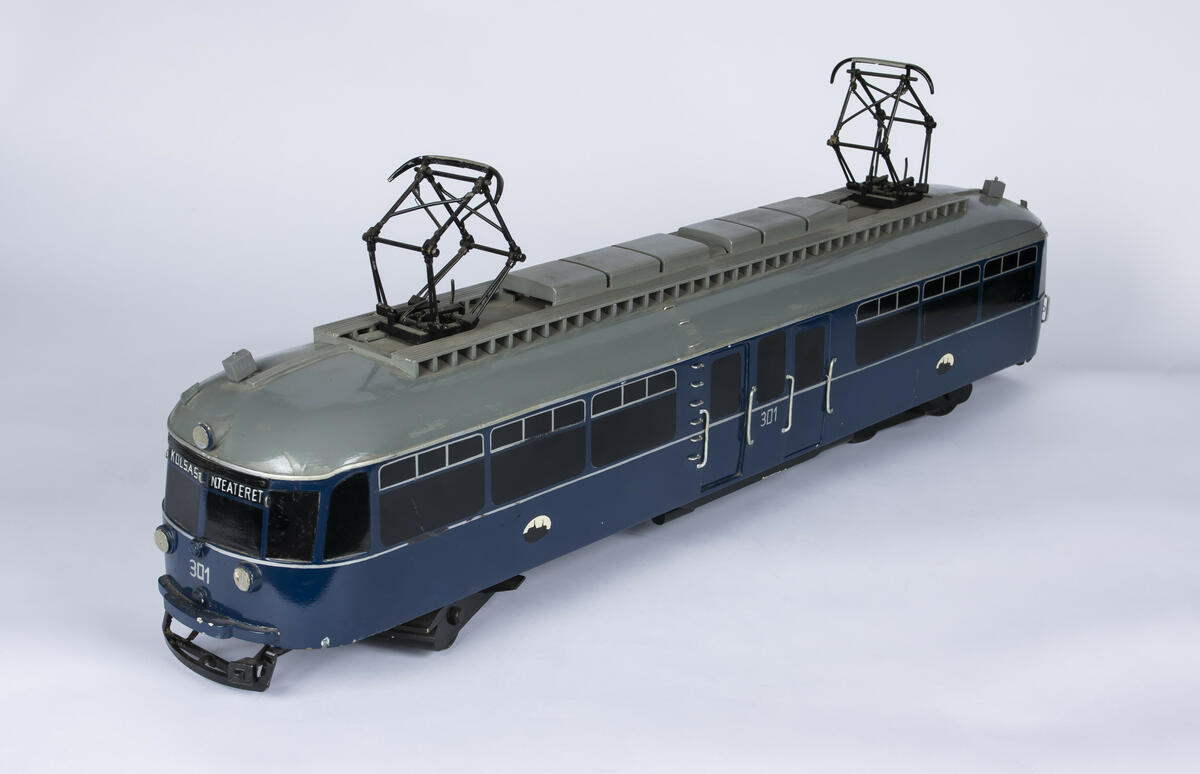 Tremodell i en mørk blå farge, med sorte vinduer og grått tak av forstadsbane fra Bærumsbanen med nr. 301. Modellen har detaljerte utskjæringer og malingsdetaljer som gjør den tro til originalen. På taket er to pantografer til kontaktledningen. 