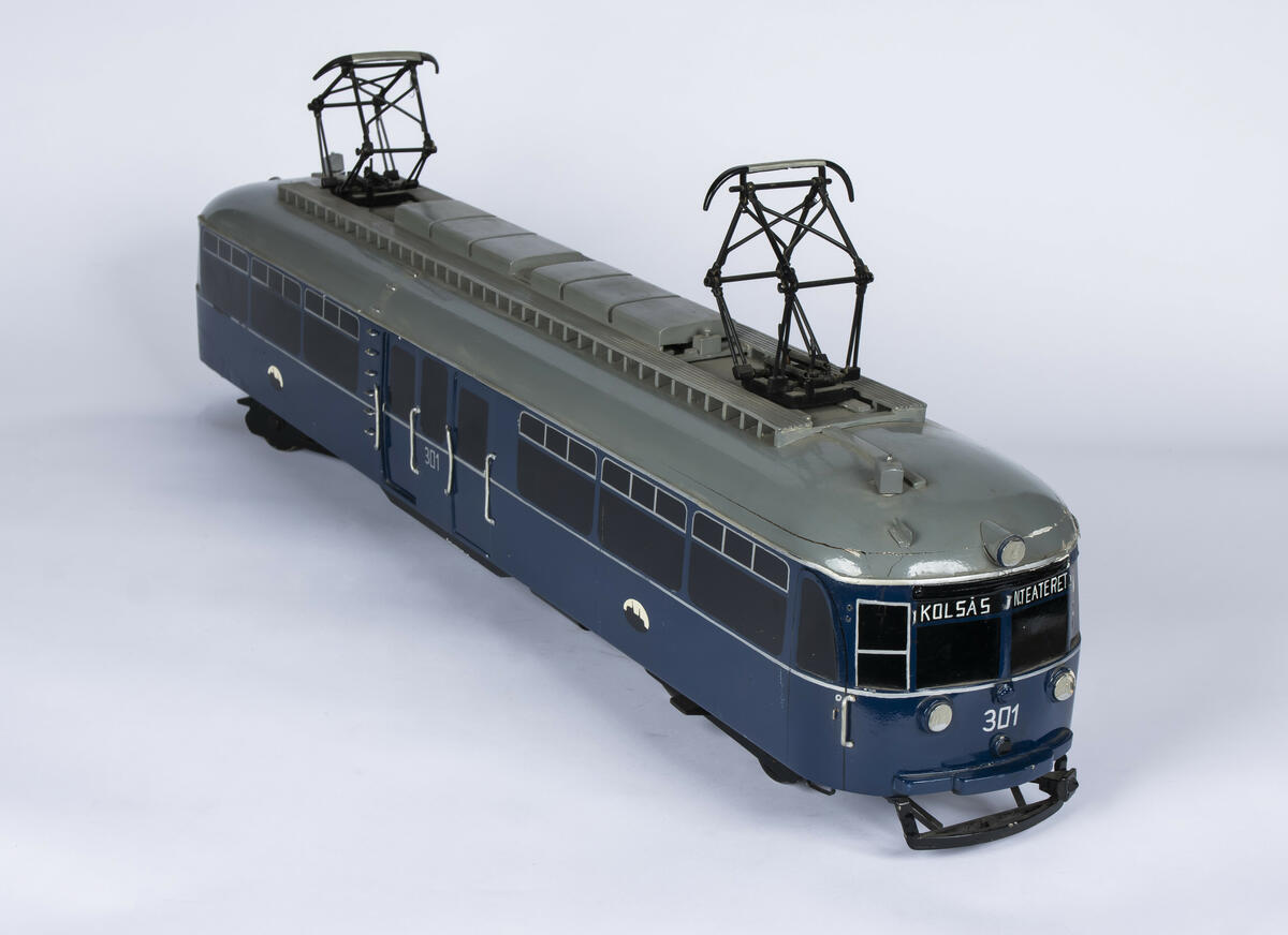 Tremodell i en mørk blå farge, med sorte vinduer og grått tak av forstadsbane fra Bærumsbanen med nr. 301. Modellen har detaljerte utskjæringer og malingsdetaljer som gjør den tro til originalen. På taket er to pantografer til kontaktledningen. 