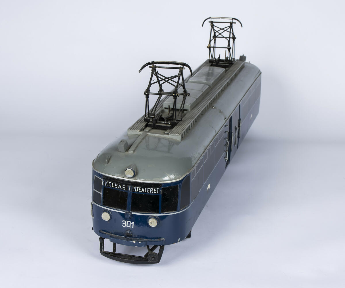 Tremodell i en mørk blå farge, med sorte vinduer og grått tak av forstadsbane fra Bærumsbanen med nr. 301. Modellen har detaljerte utskjæringer og malingsdetaljer som gjør den tro til originalen. På taket er to pantografer til kontaktledningen. 