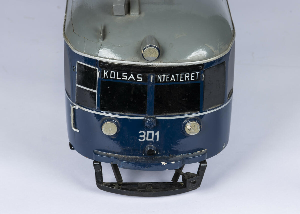 Tremodell i en mørk blå farge, med sorte vinduer og grått tak av forstadsbane fra Bærumsbanen med nr. 301. Modellen har detaljerte utskjæringer og malingsdetaljer som gjør den tro til originalen. På taket er to pantografer til kontaktledningen. 