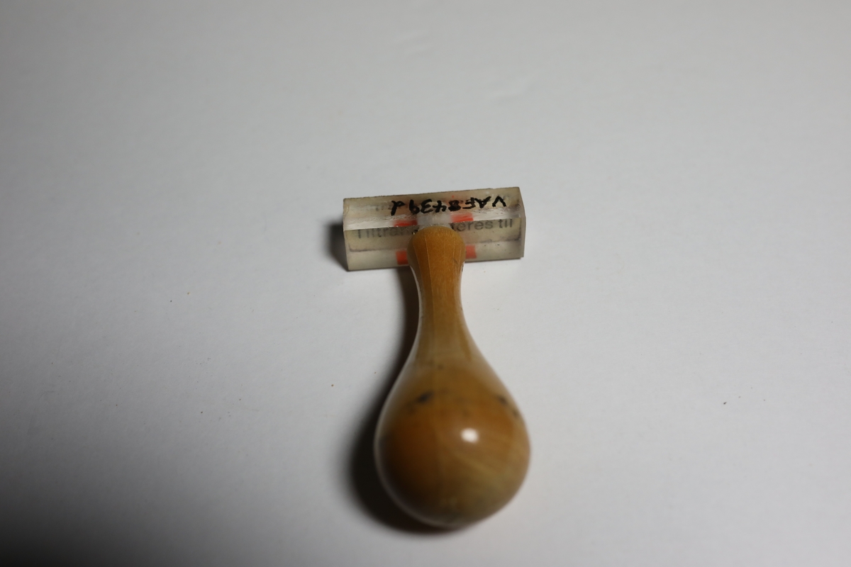 Gummistempel på rektangulært stempelhodet som er gjennomsiktig og man kan da lese hva som står under stempelet. I midten på toppen er håndtaket festet. Håndtaket smalner først svakt inn før det  vider seg ut mot den runde toppen som gir det et pæreformet form.