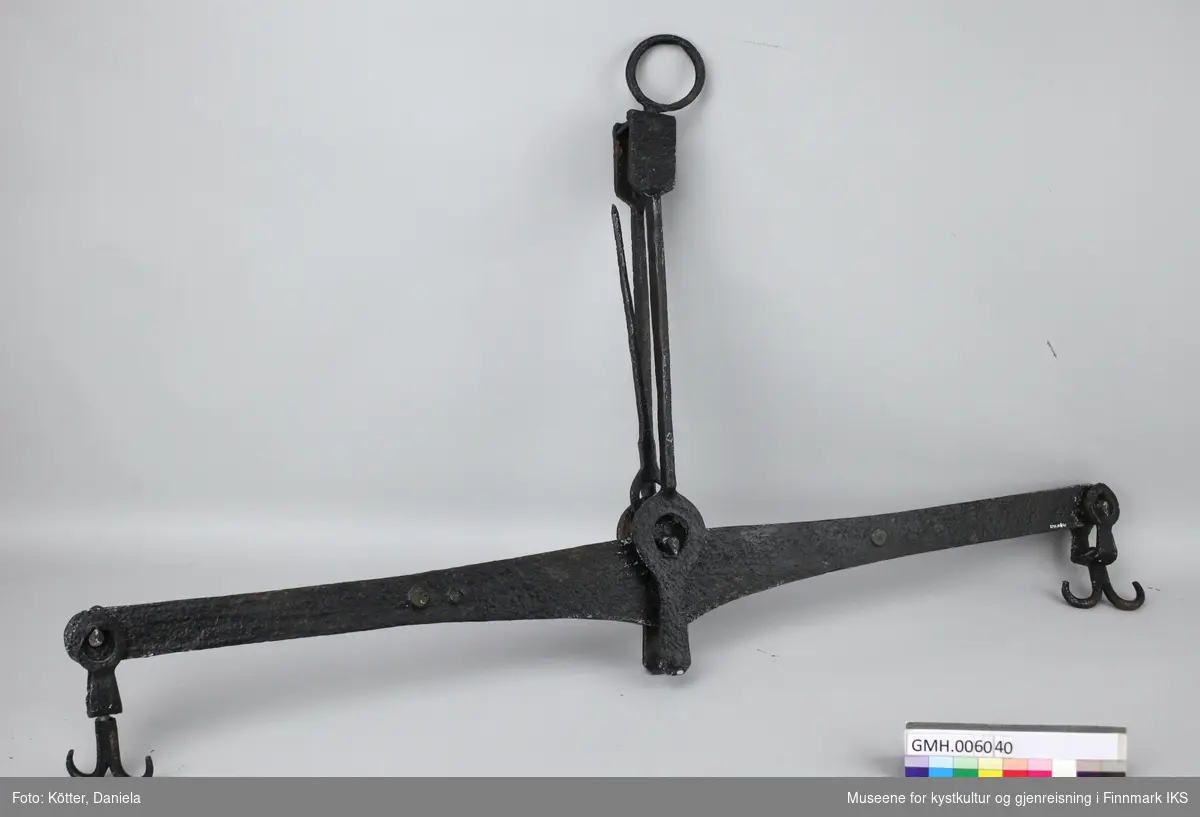 Dette er en balansevekt av svart malt jern. Det er en dobbelt krok på hver ende av vektstangen. I midten er det en peilestang.