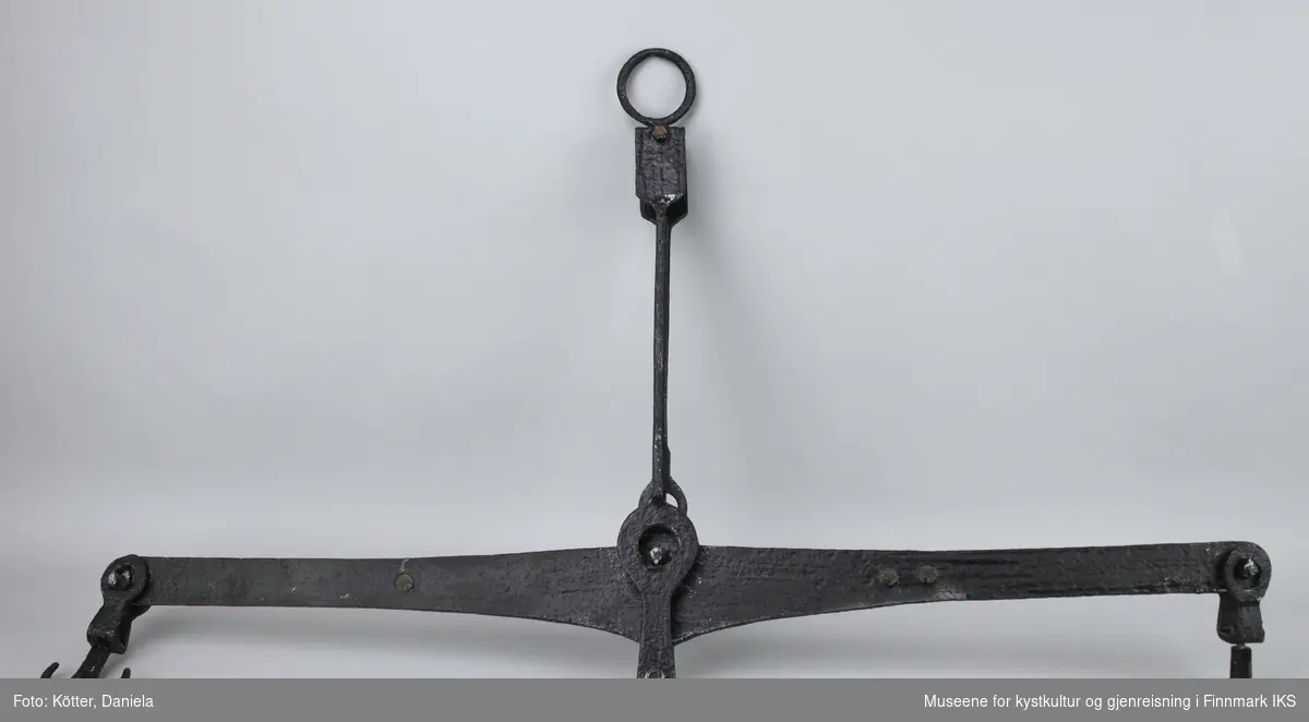 Dette er en balansevekt av svart malt jern. Det er en dobbelt krok på hver ende av vektstangen. I midten er det en peilestang.