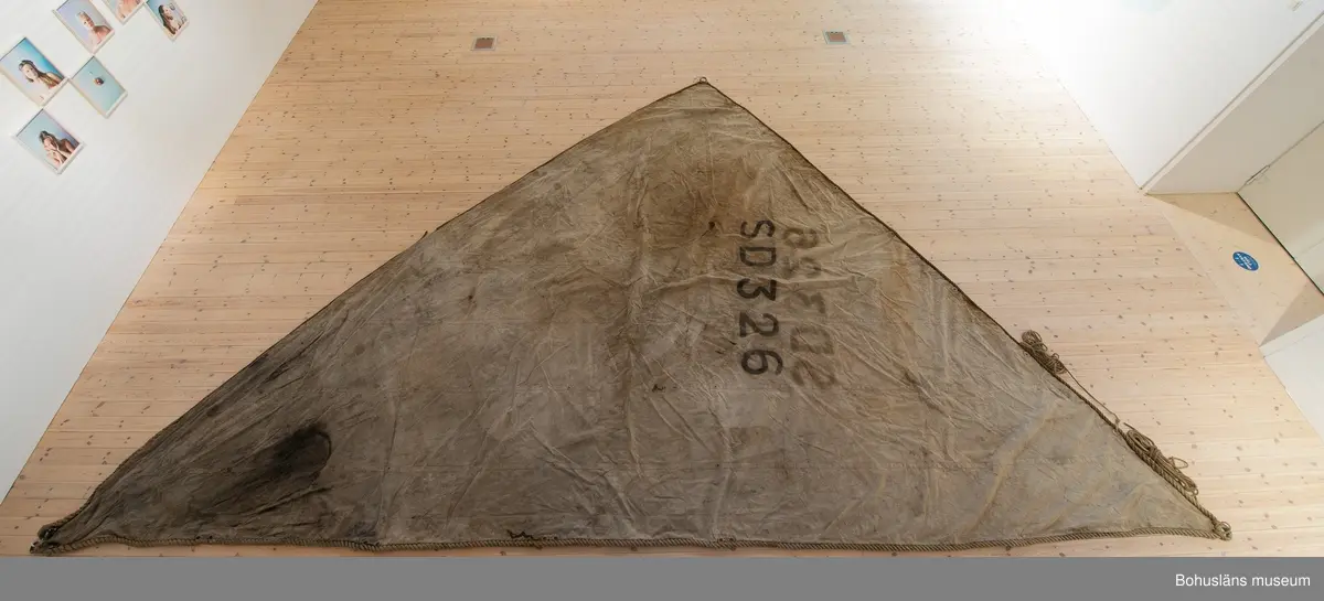 Segel Av kraftig obarkad segelduk av linne. Samtliga sidor - lik - förstärkta med tågvirke. 
Målade beteckningen SD 326 i svart. (Strömstad). 
Seglet är omsytt av ett tidigare storsegel till vanlig fiskebåt, arbetet utfört av segelmakare.