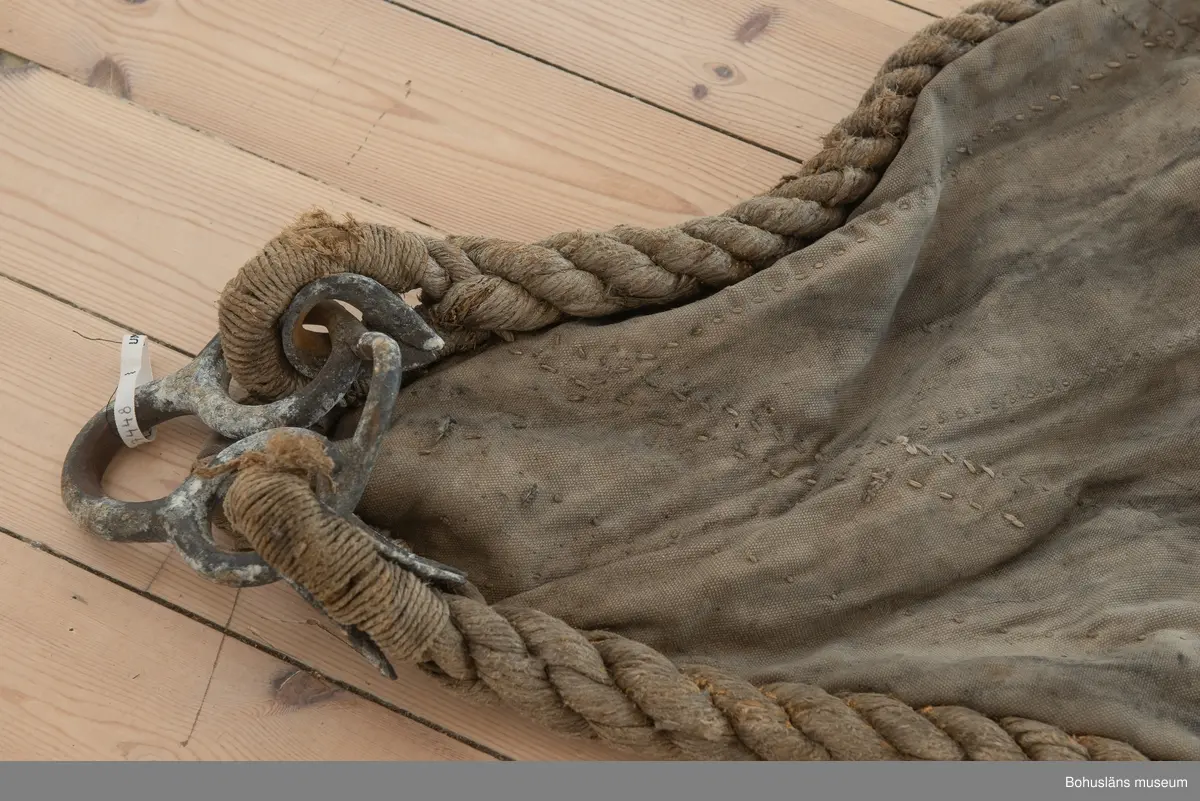 Segel Av kraftig obarkad segelduk av linne. Samtliga sidor - lik - förstärkta med tågvirke. 
Målade beteckningen SD 326 i svart. (Strömstad). 
Seglet är omsytt av ett tidigare storsegel till vanlig fiskebåt, arbetet utfört av segelmakare.