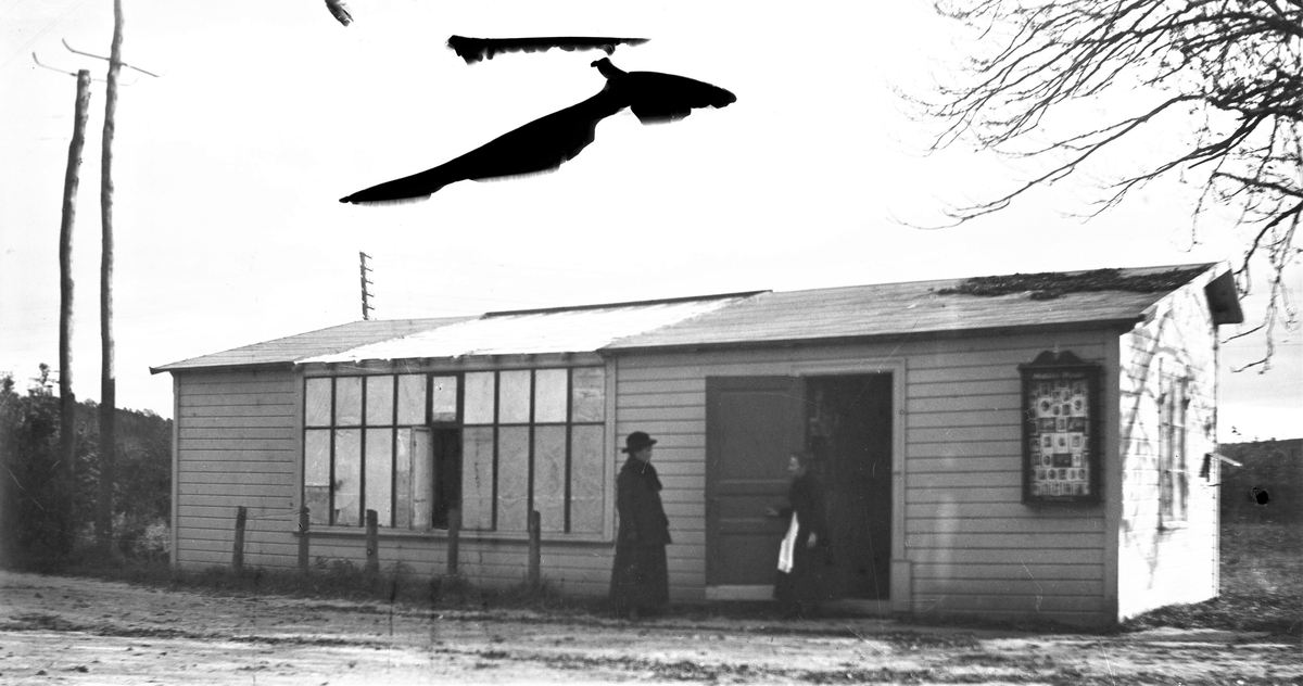 Exteriör av fotoateljén som fotograf Mathilda Ranch lät uppföra som filial på Stationsgatan i Slöinge vid 1890-talets mitt. Till höger på fasaden sitter ett skyltskåp med fotografier som ska göra reklam för ateljén, som endast var öppen sommartid. Sedan 1894 hade hon haft en ateljé inrymd i Villa Fridhem, ägd av Sven Christiansson. Sven blev föreståndare för filialen och gifte sig med Mathildas piga Anna år 1899. Annas mor Kristina Dahl var hushållerska åt Sven. I bild finns telefon- respektive elstolpar. (Skador på negativet ger stora svarta fläckar)