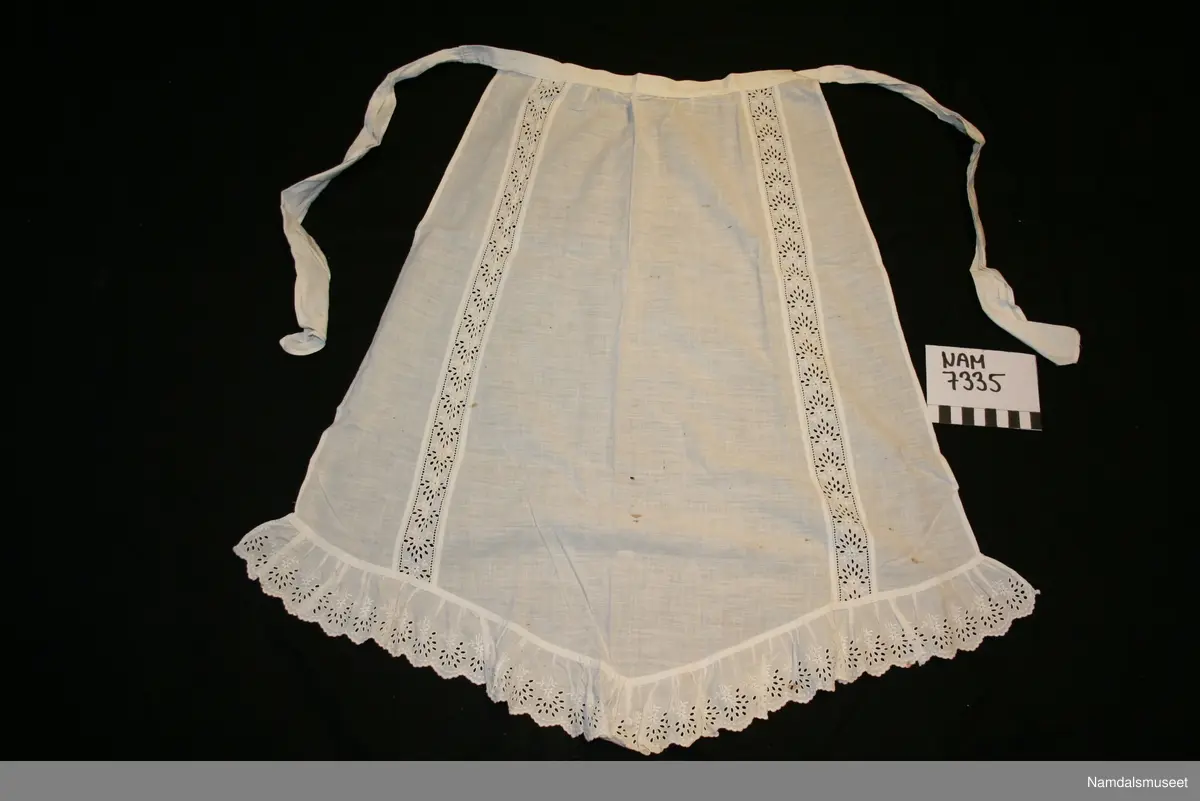 Pynteforkle med broderikant nederst og to langsgående broderistriper på selve forkleet.