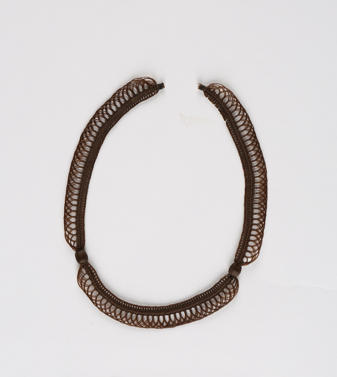 Halssmykke i kragefasong, ytterst med en gjennombrutt kant, innerst en fastere kant, begge holdt sammen på to steder av runde hårtrukne perler. Lås mangler.