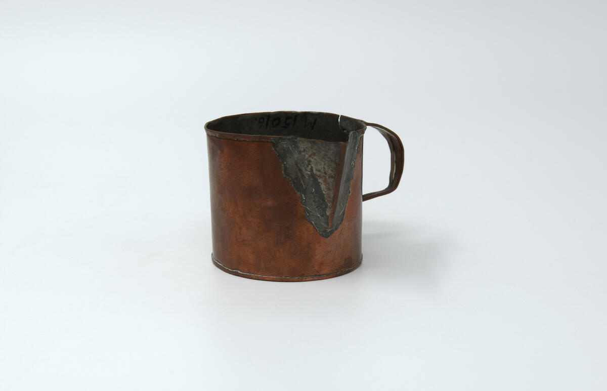 Kannans botten är rund och har rakt sidostycke med en smal fals i överkant och en pip 2,5 cm djup. Pipen är tennlödd och förtent. Handtaget är utfört i vikt plåt och fästad med tennlödning. Insidan är förtent. Botten är plan o med tennlödd fals sidostycket har slaglödd fals till höger om handtaget. Tillstånd: Överkanten är bucklig. En reva på var sida om handtaget.