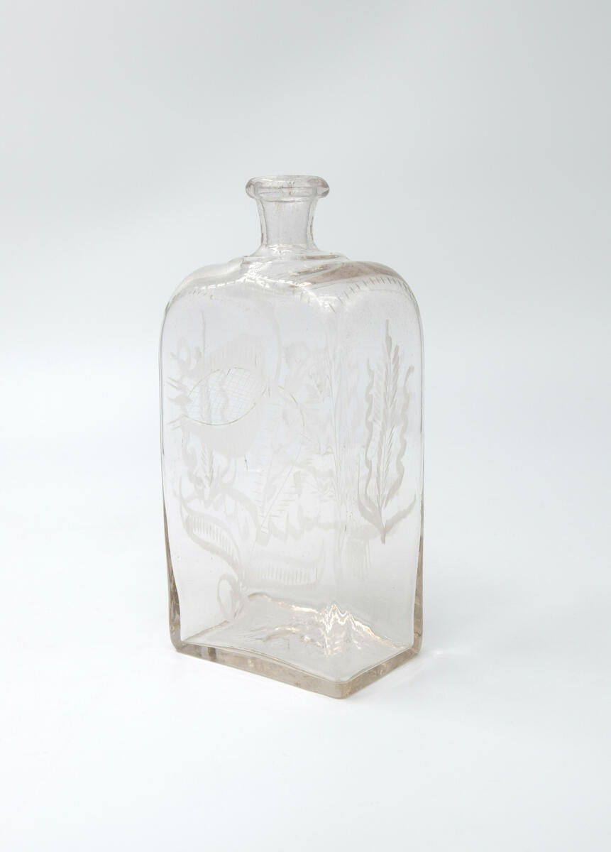 Brännvinsflaska, av glas. Rektangulärt tvärsnitt. Slipade blommor och blad.