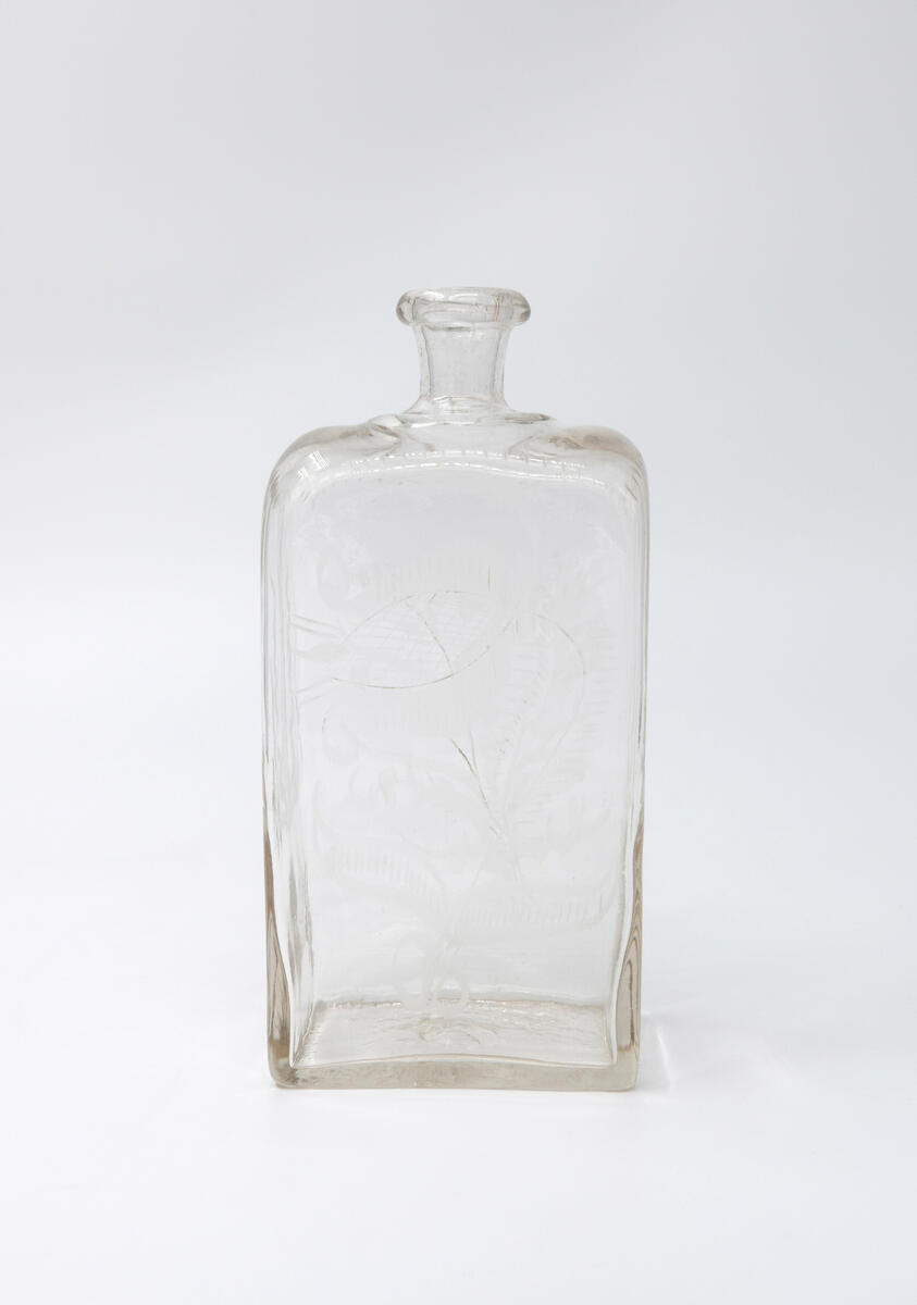 Brännvinsflaska, av glas. Rektangulärt tvärsnitt. Slipade blommor och blad.