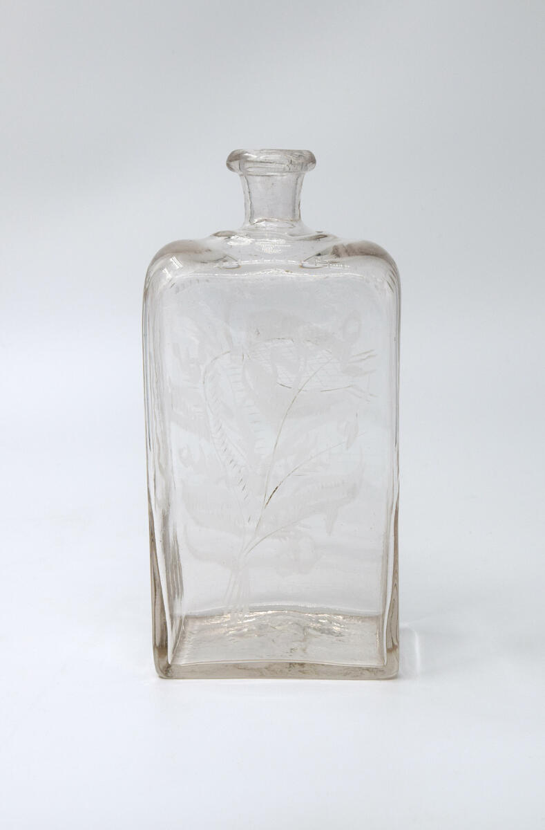 Brännvinsflaska, av glas. Rektangulärt tvärsnitt. Slipade blommor och blad.