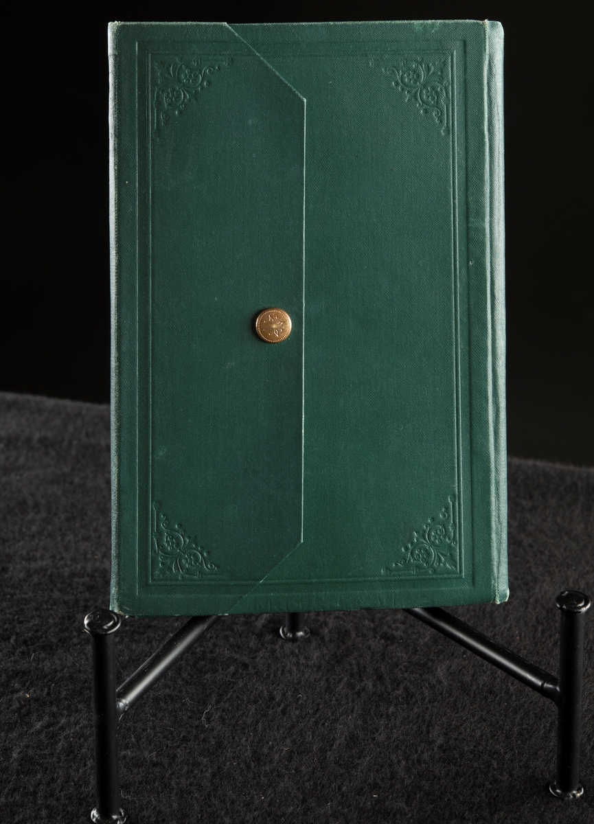 Grönt klot, med extra omslag för att stänga boken med tryckknapp på baksidan.
Präglad pärm med blommönstrad ram. Texten i guldprägling.