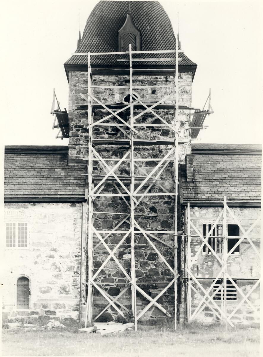 Svart-hvitt bilde med utsnitt av Austråttborgens fasade. Tårnet er midtstilt i bildet. Langs veggen, og oppover tårnet, er det satt opp et stillas av tre.