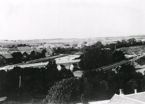 Vy över Falkenberg med järnvägen från 1886 i förgrunden och den gamla stenbron i bildens mitt. 
Bilden ingick i den av Albert Sandklef på Museet i Varberg ordnade pristävlingen om gamla hallandsbilder. (En del publicerade i boken ""Från fars till farfars tid - en bokfilm om Halland"", Utgiven 1961). Se anm. 1800-tal.