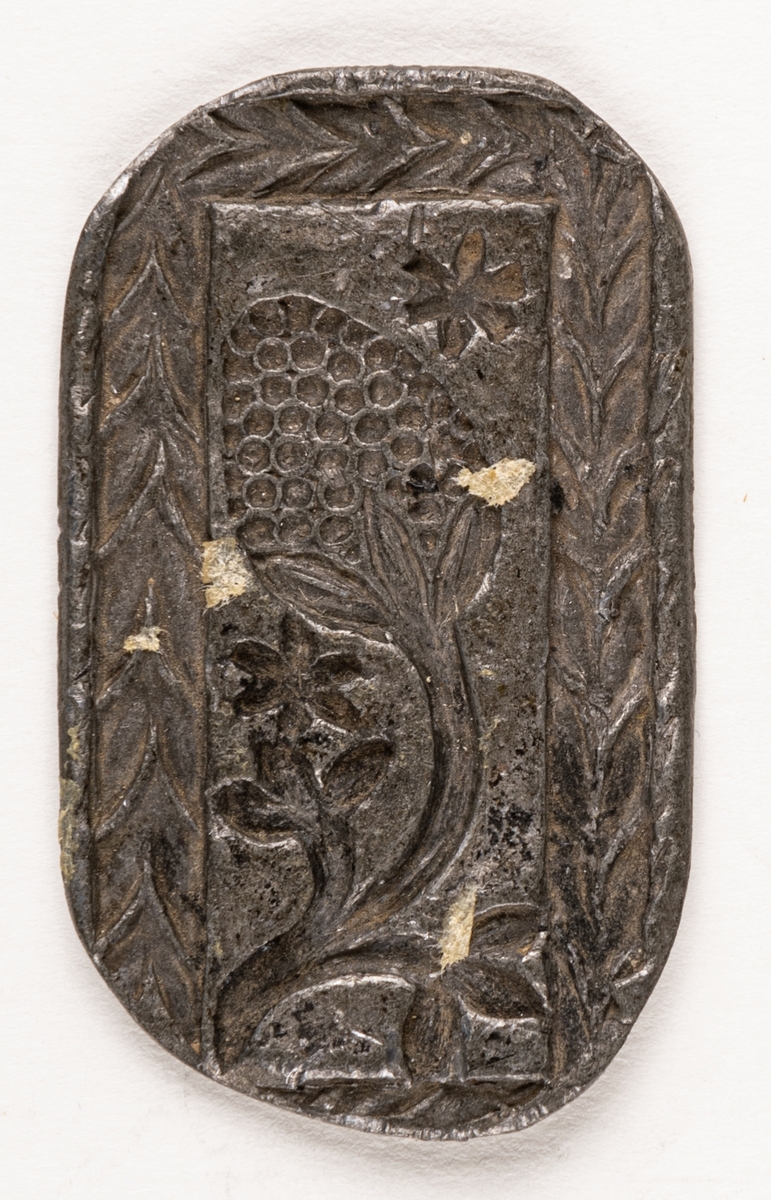 Järnstämpel från Högbo Bruk.
Prov på stämplat järn. Relief; Fruktkvist omgiven av krans m.m.