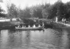 Sju personer i en roddbåt vid kanalen, Gröndal, Norrlandet, Gävle kommun 1902. Tre personer står på stranden.