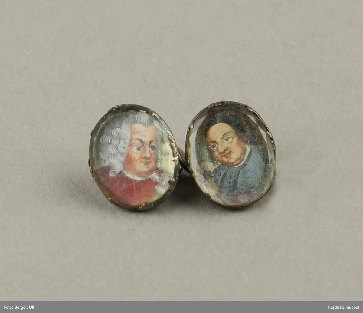Manschettknappar, två par, miniatyrer. 1700-tals mitt.  Silver, glas.
Saknar stämplar. På varje knapp ett ovalt porträtt i miniatyr i silverinfattning, baksidan räfflad, knapparna förenade två och två, på den ena föreningslänken. ”I H” i genombrutit arbete, den andra föreningslänken senare ersättning. Manschettknapparna hölls i ett rött marokäng (getskinn) etui.
(katalogiseringen gäller a-c)
