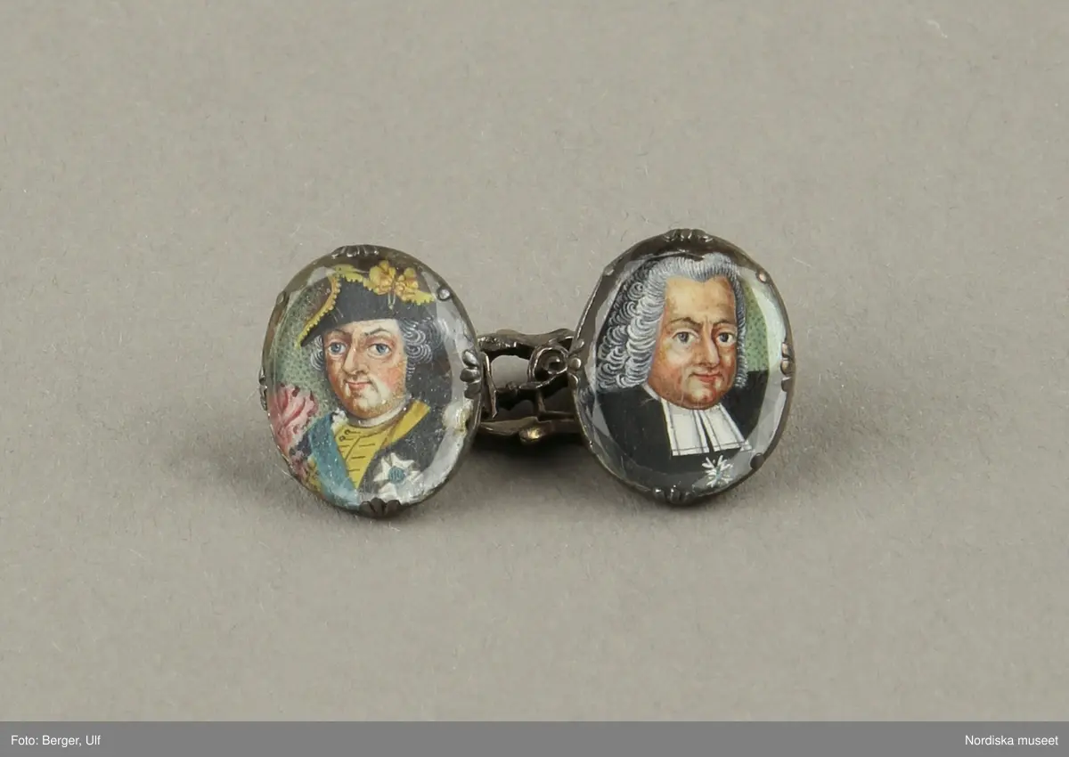 Manschettknappar, två par, miniatyrer. 1700-tals mitt.  Silver, glas.
Saknar stämplar. På varje knapp ett ovalt porträtt i miniatyr i silverinfattning, baksidan räfflad, knapparna förenade två och två, på den ena föreningslänken. ”I H” i genombrutit arbete, den andra föreningslänken senare ersättning. Manschettknapparna hölls i ett rött marokäng (getskinn) etui.
(katalogiseringen gäller a-c)
