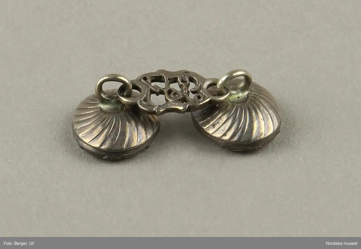 Manschettknappar, två par, miniatyrer. 1700-tals mitt.  Silver, glas.
Saknar stämplar. På varje knapp ett ovalt porträtt i miniatyr i silverinfattning, baksidan räfflad, knapparna förenade två och två, på den ena föreningslänken. ”I H” i genombrutit arbete, den andra föreningslänken senare ersättning. Manschettknapparna hölls i ett rött marokäng (getskinn) etui.
(katalogiseringen gäller a-c)