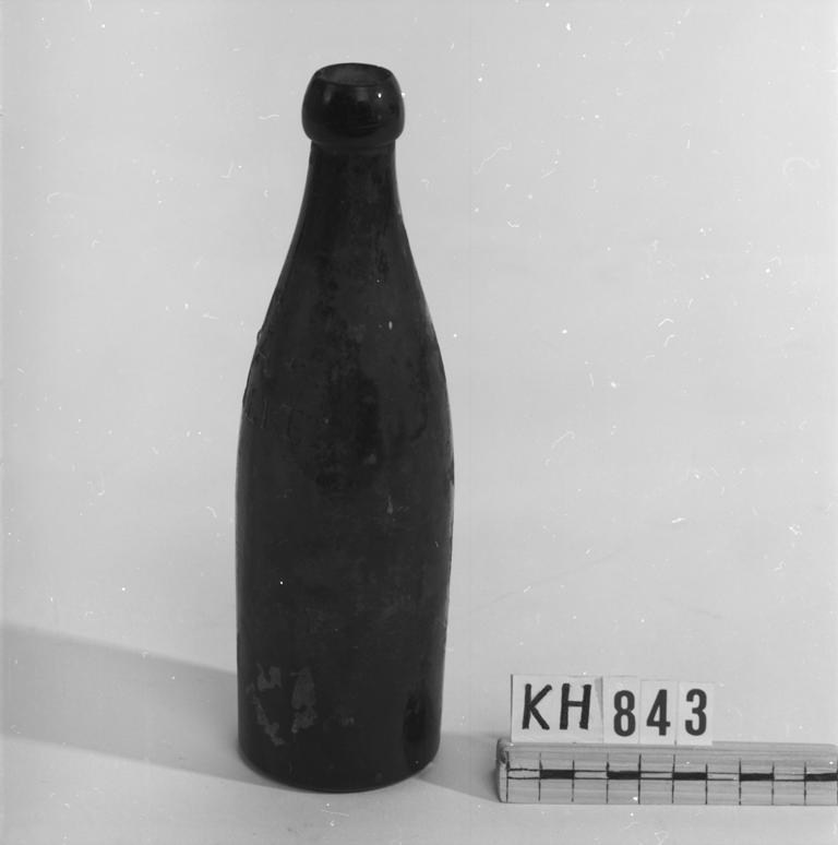 Brunt glas med kulformad mynning. Rester av kork finns kvar i mynningen.
Märkt: "Å *** 1/3 Lit." 
Märkt under botten: "Årnäs 1911 8".