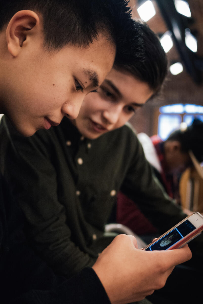 To gutter ser på en mobilskjerm, den ene i prodil og den andre forfra. Fotografi.