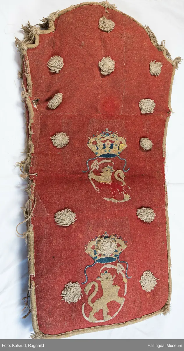 Sledepute i raudbrunt ulltøy. Pute til både sete og rygg. Ryggdelen av puta har kroneform, medan den andre enden er noko boga. To like sideflater med ca. 5,5 cm høg kant rundt heile puta. Sledeputa er trekt med raudbrunt ulltøy (plysj). Saumane er kasta saman med lys tråd, og kanta med lys gråfult toskaftvove ullband med duskar i hjørnene. Det er same type dekor på begge sidene, delvis applikert og delvis brodert i fargane lys grågult, blått og raudbrunt. Dekoren er to løver med krone, og øks med boga skaft i framføtene. Dessutan er det påsett 12 duskar av lyst grågult ullgarn, 3 av duskane på eine sida er borte. Inni puta er turka gras. Fargane er ein del falma, og puta har nokre hol av ulik storleik. Noko av kantinga rundt er òg manglande. 