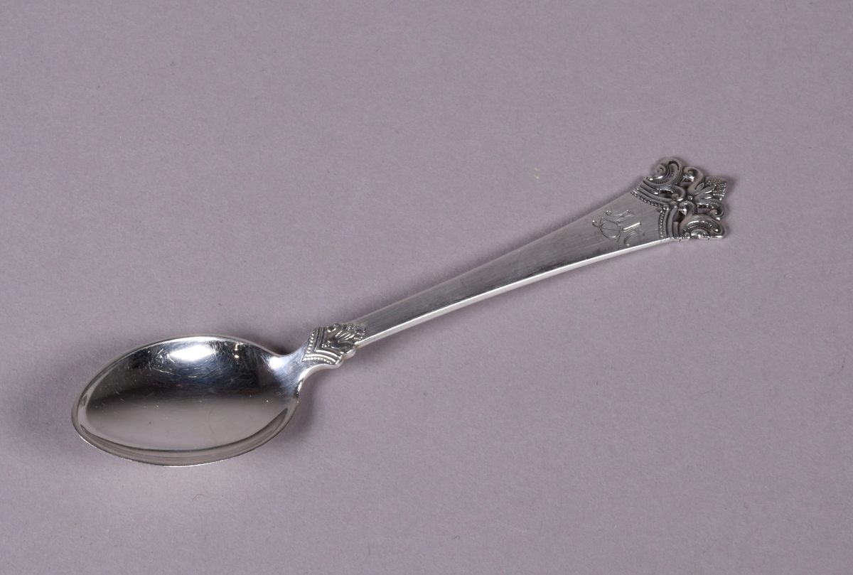 Skje av sølv med støpt dekor i enden av skaftet og ved overgang til skål. Mønsteret ved enden er gjennombrutt med fire rektangulære hull.