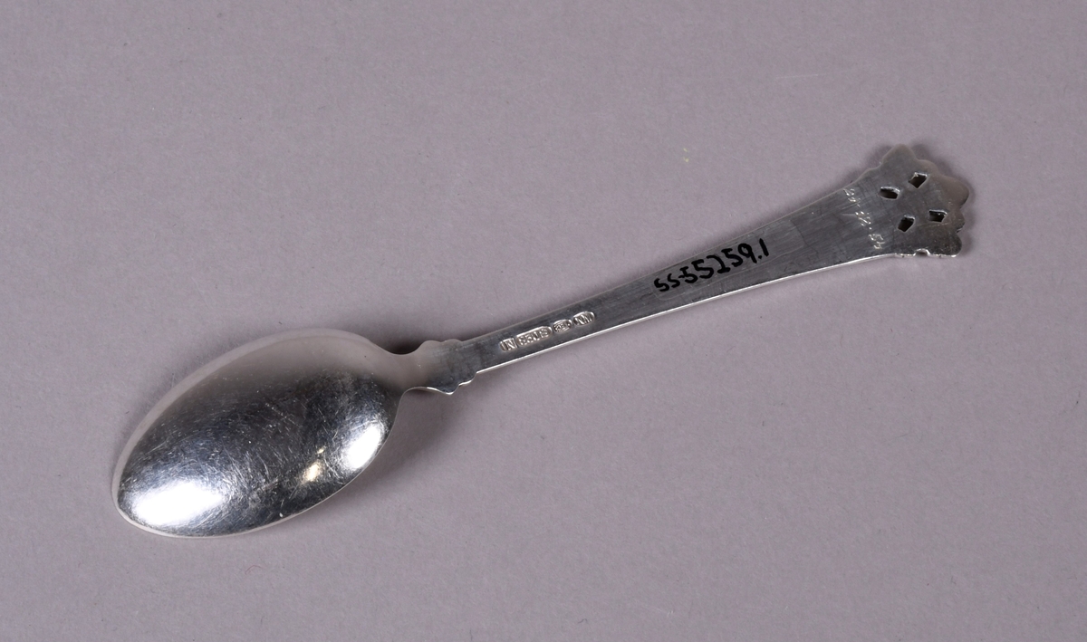 Skje av sølv med støpt dekor i enden av skaftet og ved overgang til skål. Mønsteret ved enden er gjennombrutt med fire rektangulære hull.