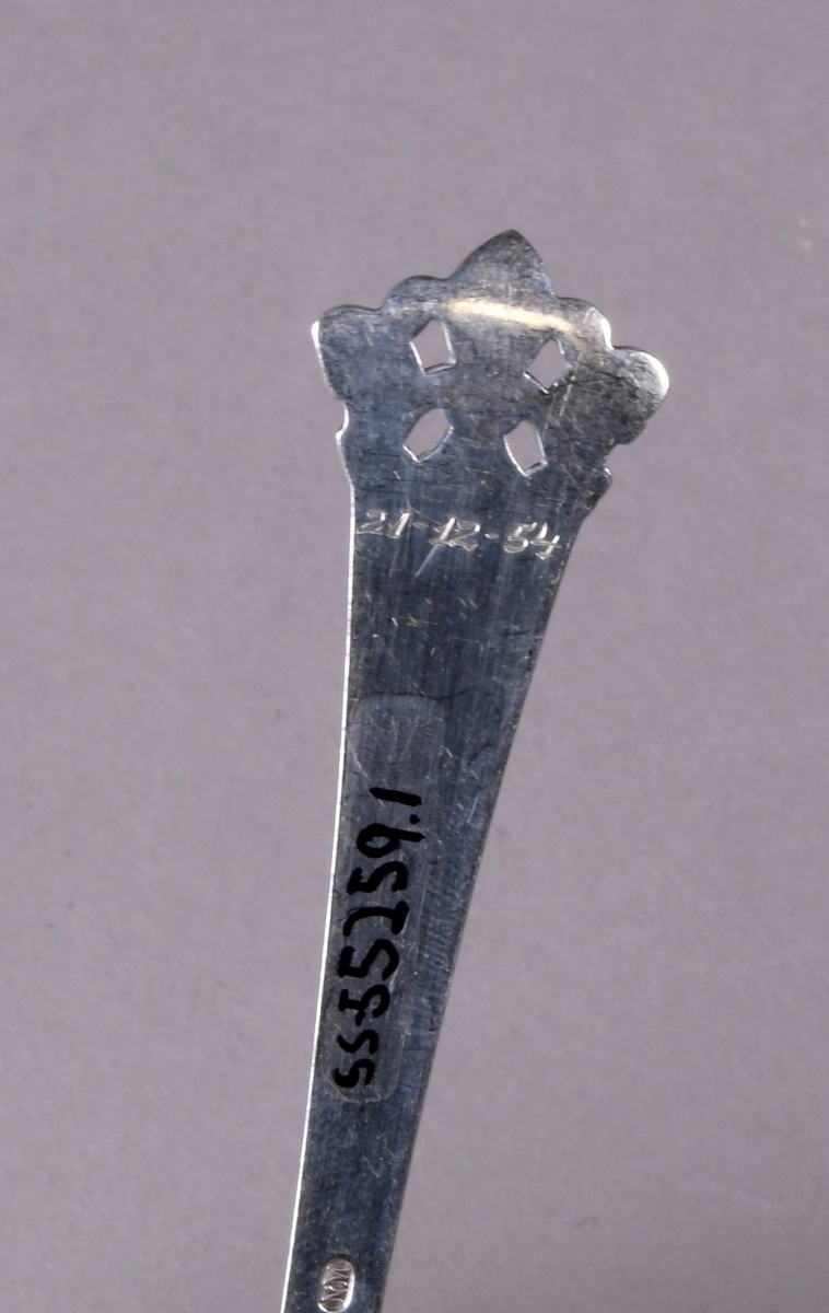 Skje av sølv med støpt dekor i enden av skaftet og ved overgang til skål. Mønsteret ved enden er gjennombrutt med fire rektangulære hull.