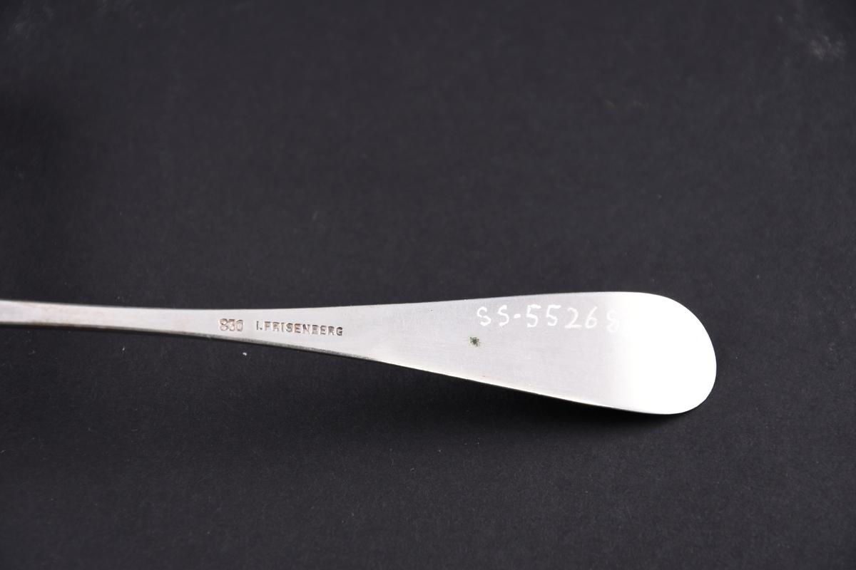 Serveringsskje av sølv. Skaftet er dekorert med innsenket mønster i form av et skjold med planteblader under og over.
