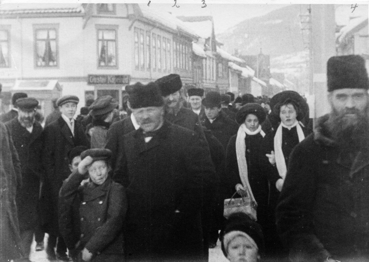 Stillbilde fra Albert Hougners film fra Storgata, Lillehammer 1912. Menneskemengde, hvor blant annet man kan se Byggmester Høgsveen, kirketjener Joakim Berg, Murer Hagen også kalt "Tambuin" og Cigarmureren" og dreier Edvard Olsen. I Bakgrunnen Gustav Kapelruds forretning i Storgata 86