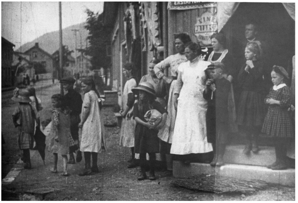 Stillbilde fra Albert Hougners film fra Storgata, Lillehammer 1912. Inngangen til Storgata 115, S. Halvorsens kolonial. Skilt utenfor med reklame for "Vine fra P.A. Larsen". Helt i bakgrunnen Storgata 132-136