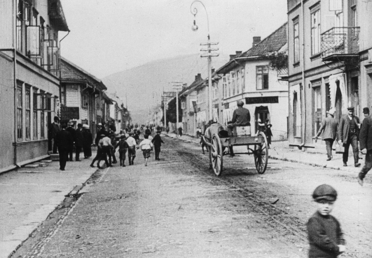 Stillbilde fra Albert Hougners film fra Storgata, Lillehammer 1912. Hjørnet Storgata/Jernbanegata med Storgata 56 til venstre og 55 (senere 57) til høyre. Hest med vogn.