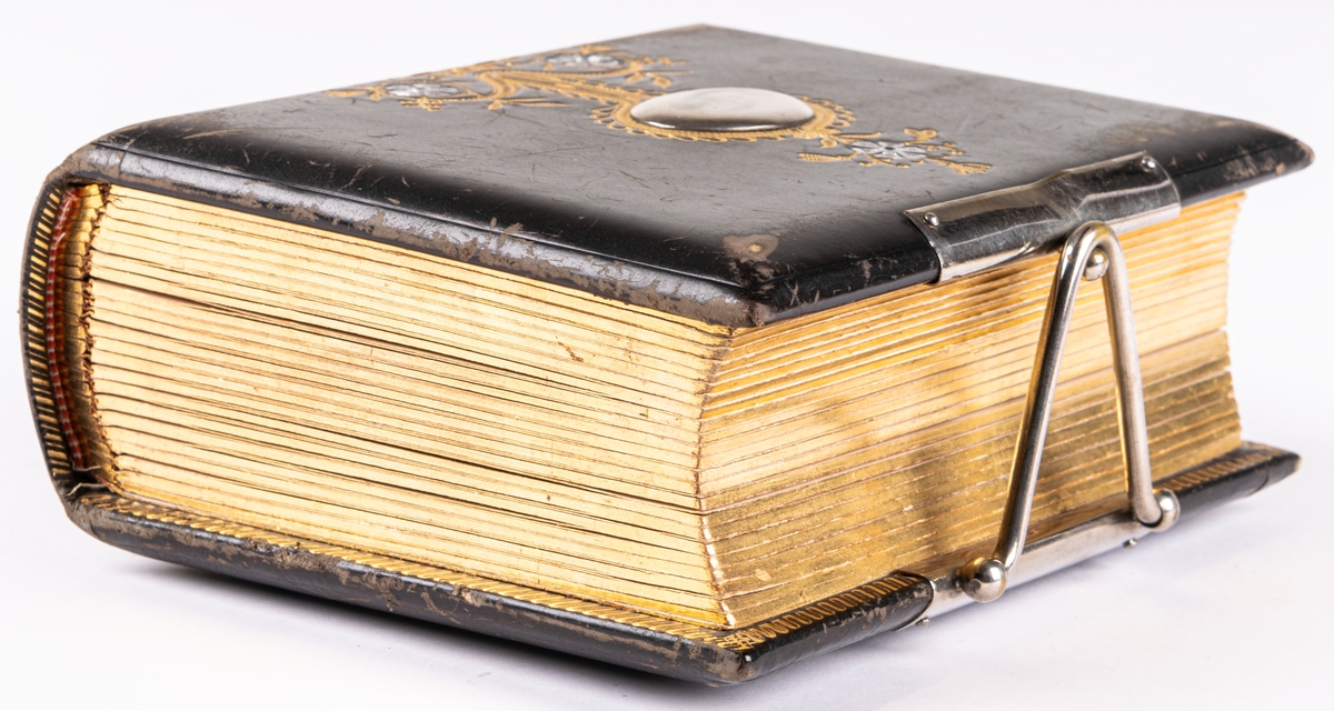 Fotoalbum, i svart papp. Dekor med gyllene ornamentik och plåtmedaljong samt lås. Albumet har tillhört Gustaf Swedlund.