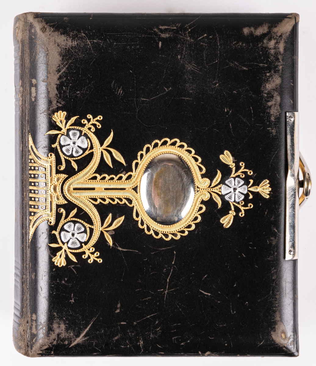 Fotoalbum, i svart papp. Dekor med gyllene ornamentik och plåtmedaljong samt lås. Albumet har tillhört Gustaf Swedlund.