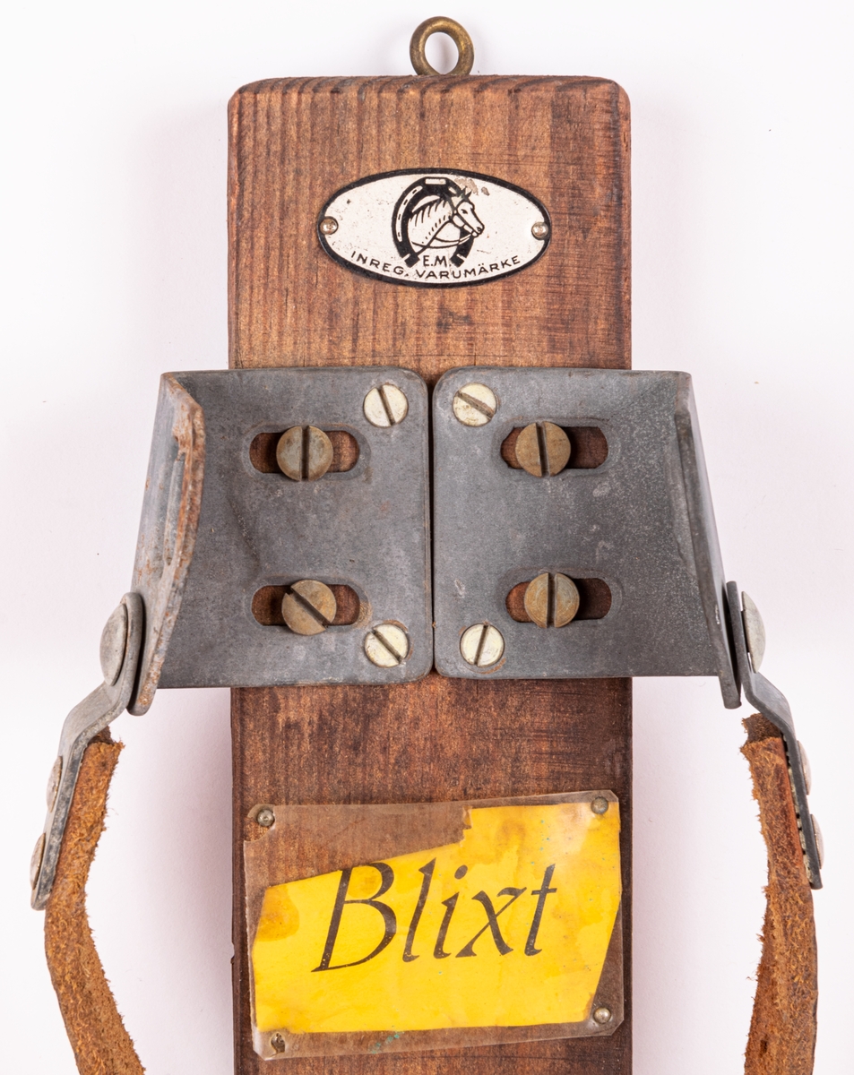 Skidbindningsprov. Metall på trä. Läderemmar. På ovansidan genomskinlig rektangulär plastskiva över gul etikett med text "Blixt". Elof Malmbergs firmamärke i metall.