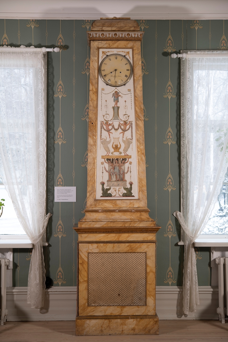 Spelur. Ett rektangulärt trästycke med orgelverk samt sen-gustavianskt (Masreliez-stil) dekor målad i guldaktig marmorerad oljefärg. 
1. Fodral
2. Ur
3. Huv
4. Låda för valsar
5-17 valsar med olika musikstycken.
Mått: Uret, tre delar: höjd 3010 mm varav toppen 310 mm, mitten 1720 mm, nedre 980 mm. Förvaringslåda 1350x490x360 mm.