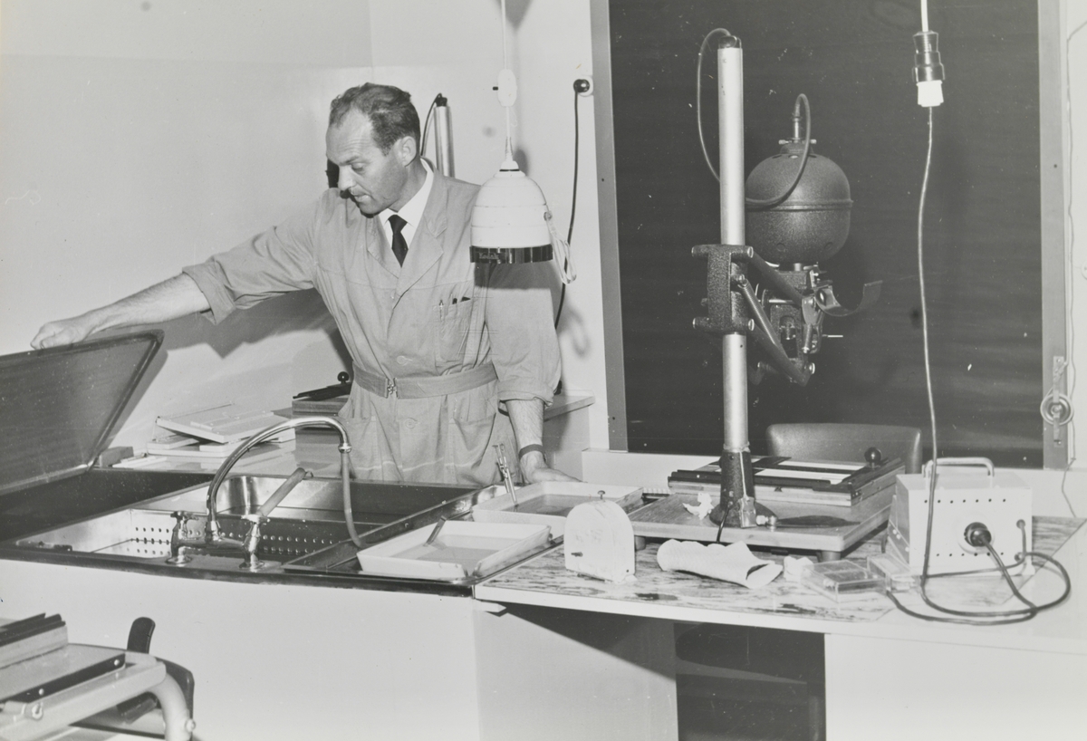 En mann i labfrakk står bak en benk med utstyr for fotofremkaling.