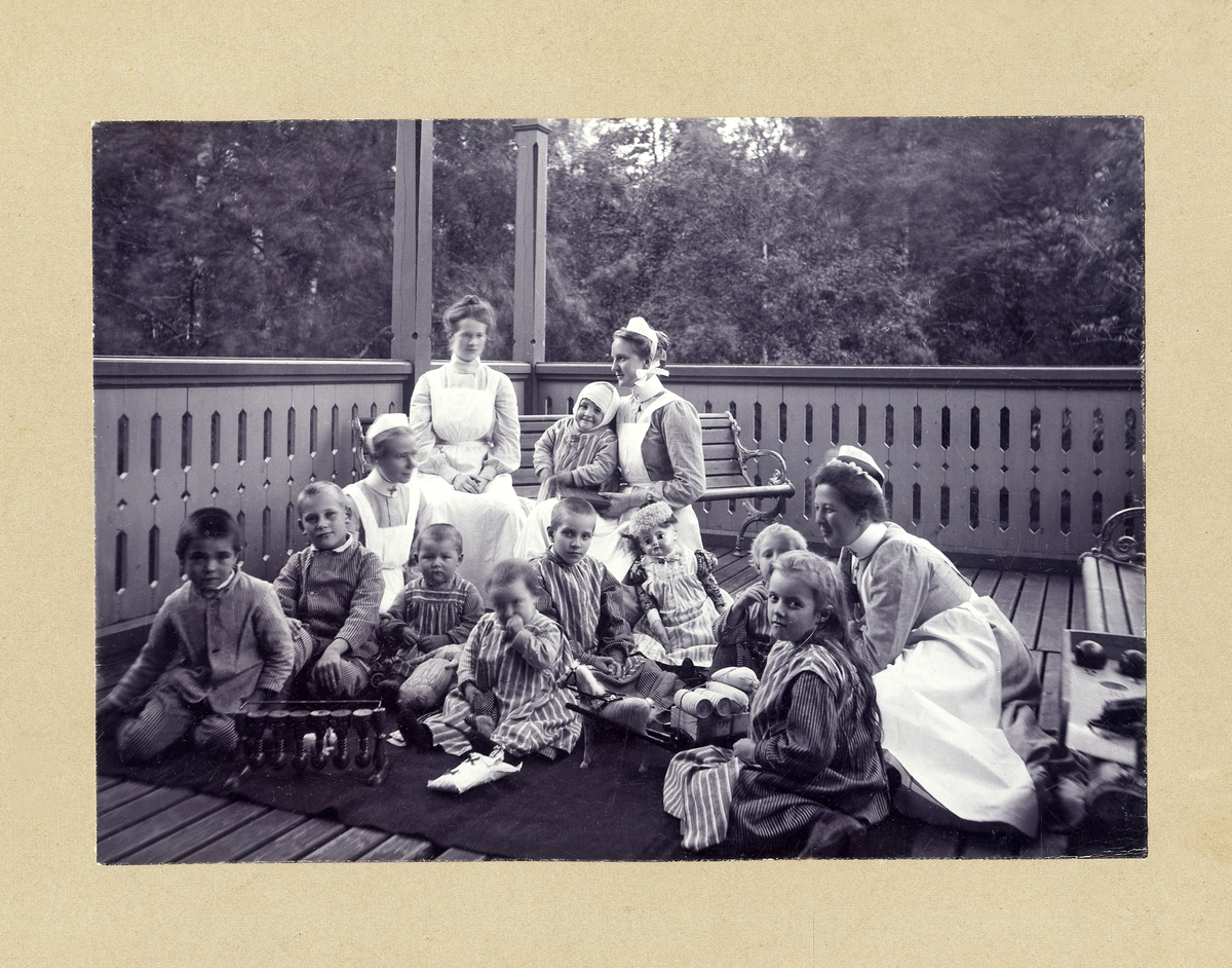 Några sjuksköterskor med en grupp sjuka barn på en veranda vid Växjö lasarett, ca 1910.