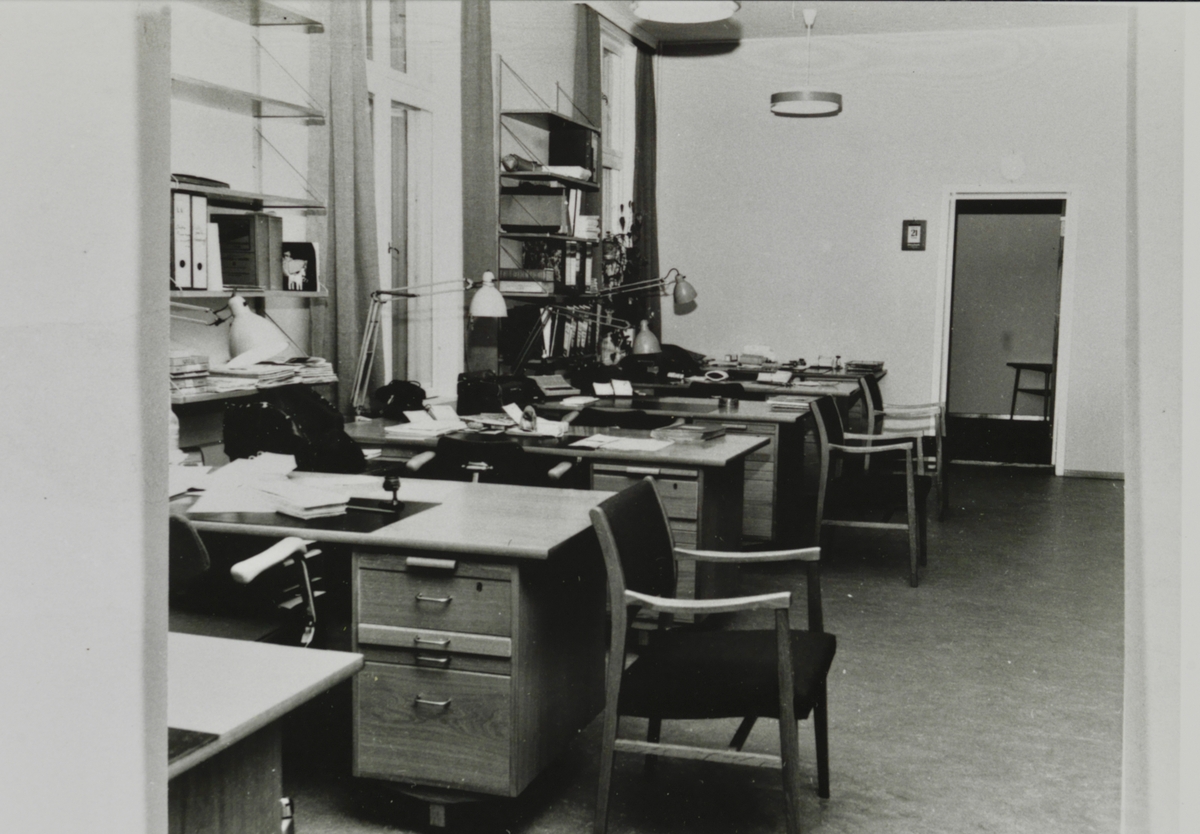 Kontorlokale med flere skrivebord og bokhyller.