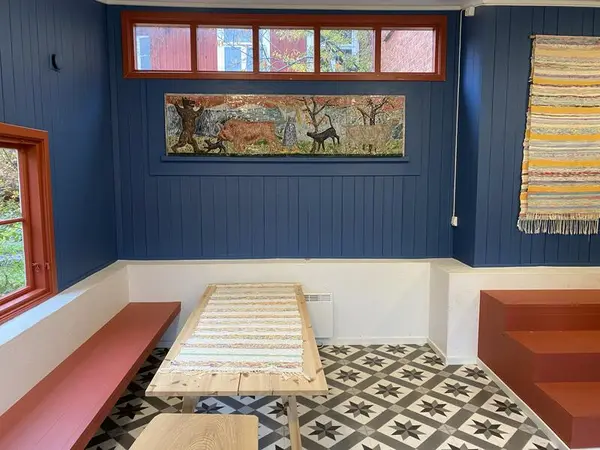 Rom med blå vegger, kunst på veggen, bord og benker står på gulvet.