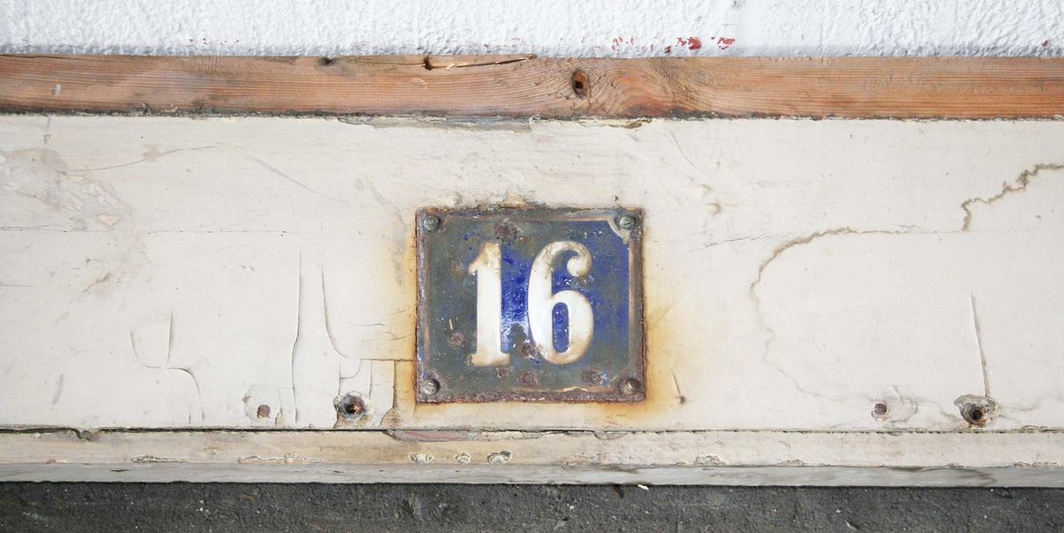 Pilastrar med räfflor, överst cirkelrund dekor, nedanför denna list med tandsnitt. Krönlist med tandsnitt. Därunder slätt parti med husnumret "16" i vitt på blå emalj. Under siffrorna fönster, grönmålat med oregelbunden ruta i mitten, på vardera sidan 3 rutor med skuret kryss. Under fönstret tandsnittsbård. Tröskel.

Hör till dubbeldörr BM 64754. Teckning på det gamla registerkortet.

Proveniens: Från ett rivet hus (1965) på Lilla Brogatan 16, Borås.